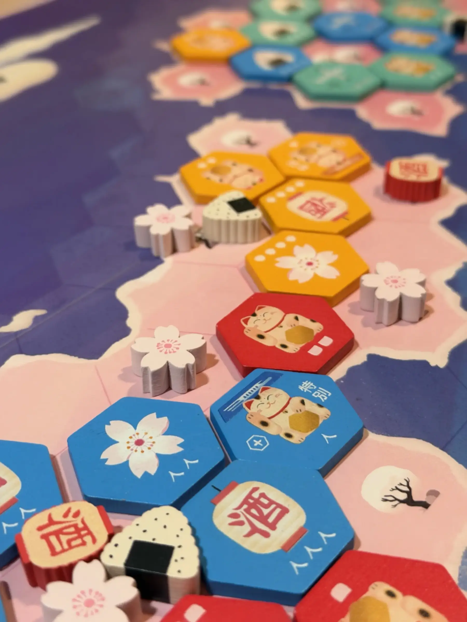 Wooden hexagon tiles with cherry blossoms, lucky cats and lanterns on a pink and purple game board