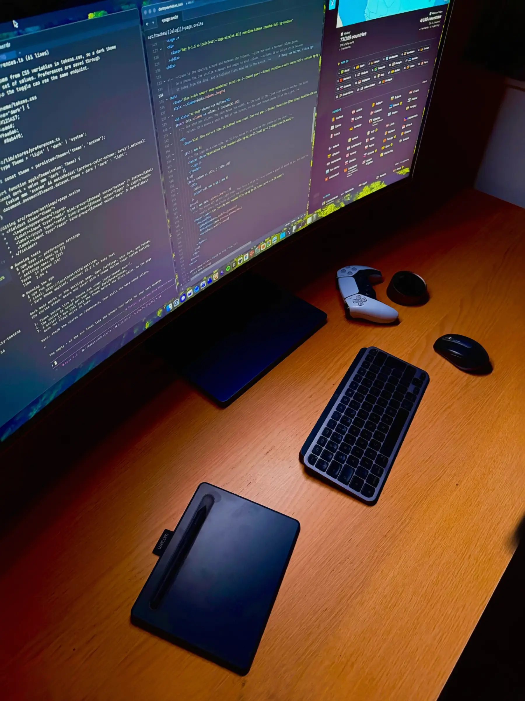 A wide curved monitor seen from the side shows program code, above a wooden desk with a keyboard, mouse, drawing tablet and game controller