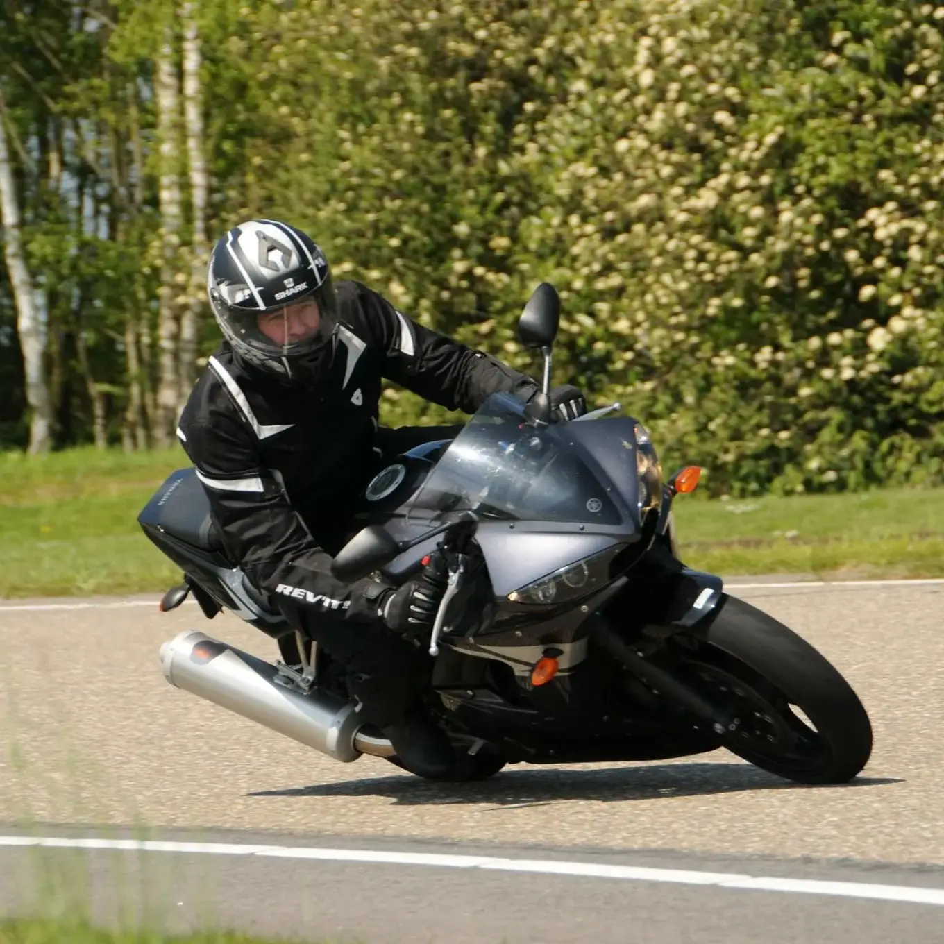 A rider in a black suit leans a black Yamaha sports bike into a corner